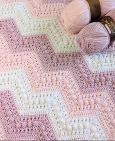 two balls of yarn sitting on top of a pink and white crocheted blanket