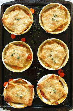 several small pies are sitting on top of a baking pan with carrots and herbs