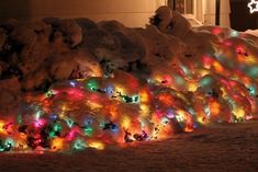 a bunch of lights that are on the side of a snow covered hill in front of a house