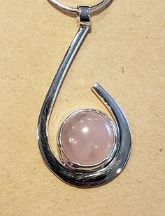 I created this elegant small pendant by hand fabricating Sterling Silver into a wrap around design holding a Pink Rose Quartz Cabachon.  The Rose Quartz is 12 mm round stone.  This piece can be worn casually or in a more formal outfit.  This pendant is about 1-1/2 inches long by 3/4 inch wide.  I am including a Sterling Silver 18 inch long 8 sided Snake Chain so it can be worn  immediately. Modern Round Cabochon Necklace, Modern Cabochon Necklace, Modern Wire Wrapped Round Jewelry, Modern Round Wire Wrapped Jewelry, Modern Cabochon Jewelry, Modern Jewelry With Round Cabochon Pendant, Wire Wrapped Rose Quartz Round Jewelry, Modern Cabochon Round Pendant Jewelry, Modern Cabochon Round Pendant