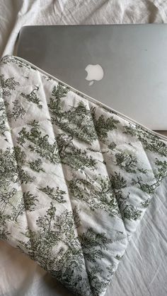 an apple laptop computer sitting on top of a white bed next to a quilted pillow