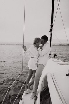 a man and woman kissing on the deck of a sailboat in the ocean, black and white photo