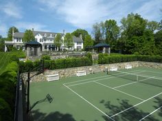 an aerial view of a tennis court in front of a large house with trees and bushes