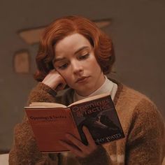 a woman sitting at a table reading a book with her hand on her head and looking down