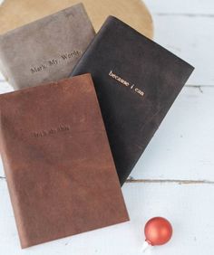 three personalized leather notebooks sitting next to a christmas ornament