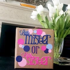 a box with some flowers in it sitting on a table next to a sign that says little mister or little sister