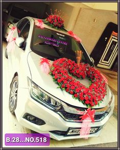 a white car with red flowers on the hood and wreaths in front of it