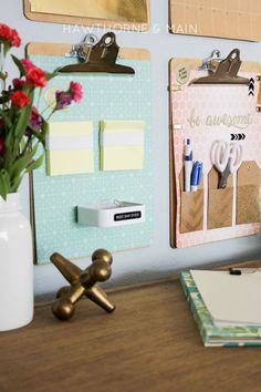 a wooden desk topped with lots of clipboards and magnets next to a vase filled with flowers