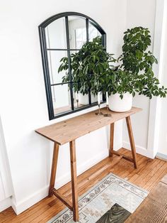 a wooden table topped with a potted plant next to a mirror on the wall