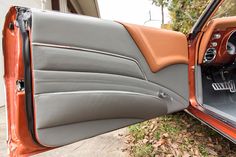 the interior of an orange and gray car with its door open, showing it's dashboard