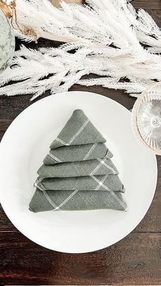 a white plate topped with four napkins on top of a wooden table next to dried plants