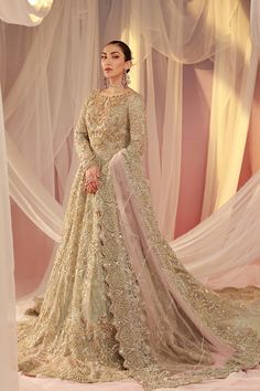 a woman standing in front of a white backdrop wearing a gold gown with sheer drapes