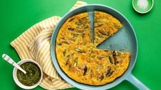 an omelet is sitting on a green table next to a bowl and spoon