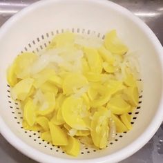 a white colander filled with peeled bananas on top of a metal sink countertop