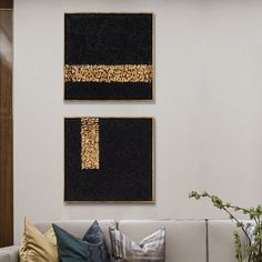 two black and gold paintings hang on the wall above a white couch with decorative pillows