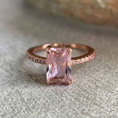 an engagement ring with a pink sapphire stone and diamonds on the band, sitting on a rock