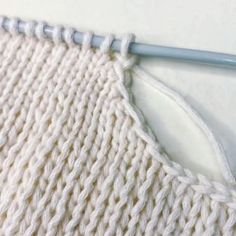 a close up of a knitting stitch on a piece of white knitted fabric with a blue crochet hook