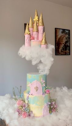 a three tiered cake with pink frosting and gold crown on top, surrounded by fluffy clouds