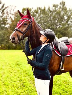 a woman standing next to a brown horse on top of a green grass covered field