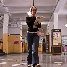 a woman walking through a building holding a pink purse and looking at papers on the floor