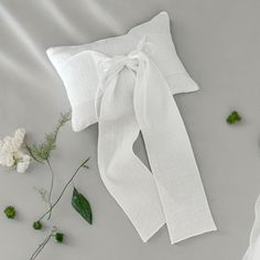 a white bow tie laying on top of a pillow next to some flowers and leaves