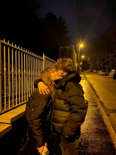 a woman standing on the side of a road at night with her arms wrapped around her body