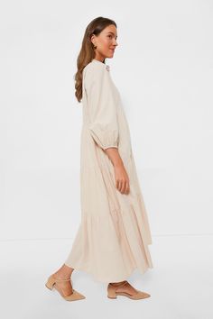 Featuring a tiered maxi skirt combined with puff sleeves in a creamy tan color, the Sandstone Mabel Dress is perfect for three seasons a year, ready to quickly become a closet staple. With a collared neckline and half front placket, this effortless piece evokes a sophisticated, relaxed feel. This no fuss maxi can be worn all day from school drop offs and errands to dinners with friends, making your day a breeze with this easy silhouette. Style this neutral, yet striking number with heels and you Cream Maxi Dress With Ruffle Hem, Feminine Beige Maxi Dress With Ruffle Hem, Beige Feminine Maxi Dress With Ruffle Hem, Spring Beige Tiered Skirt Maxi Dress, Beige Ruffled Tiered Midi Dress, Cream Tiered Midi Dress With Ruffle Hem, Spring Tiered Maxi Dress With Voluminous Skirt, Modest Beige Maxi Dress, Elegant Beige Maxi Dress With Ruffle Hem