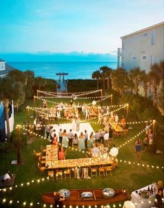 an aerial view of a wedding reception on the lawn by the ocean at dusk with string lights