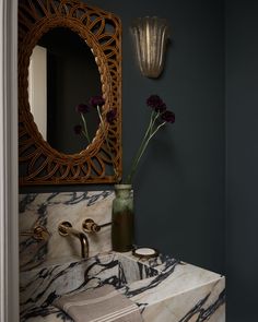 a bathroom sink with marble counter top next to a mirror and vase filled with flowers