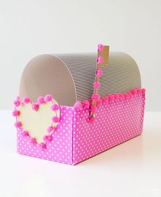 a pink and white box with a heart shaped decoration on the front, sitting on a table