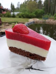 a piece of cake on a white plate with a strawberry on top and water in the background