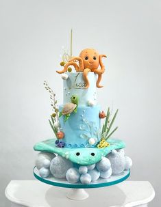 a blue cake with an octopus on top and sea animals on the bottom is sitting on a white pedestal