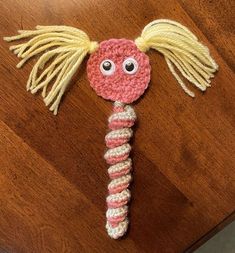 a pink and white crocheted toy with blonde hair on top of a wooden table