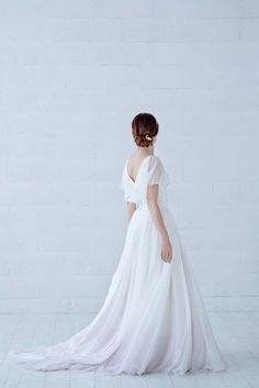 a woman in a white wedding dress standing against a wall with her back to the camera