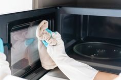 a person in white gloves cleaning an oven with a micro wave towel and cloth on it