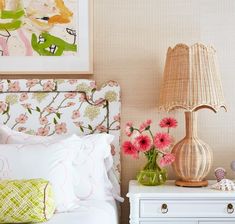 a white bed topped with pink flowers next to a night stand and lamp on top of a dresser