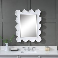 a white bathroom vanity with a large mirror above it and a vase on the counter