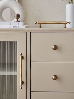 a white dresser with gold handles and knobs on it's drawers next to a book shelf