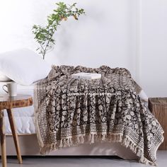 a bed with a blanket on top of it next to a table and potted plant