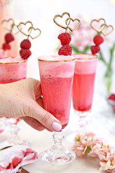 three glasses filled with raspberry drink and topped with gold heart shaped strawberries