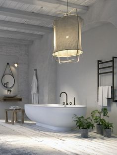 a white bath tub sitting under a light fixture in a bathroom next to a plant