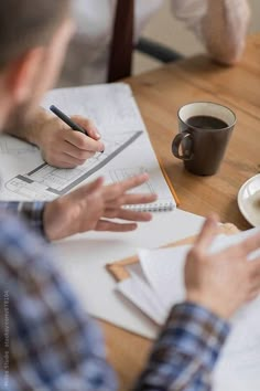 two people sitting at a table with papers and coffee in front of them, one person is writing