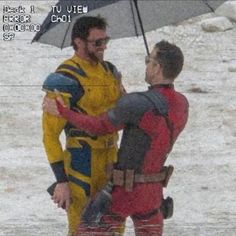 two men dressed as deadpools in the snow with an umbrella over their heads