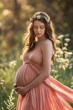 a pregnant woman in a pink dress standing in the grass with her hands on her belly