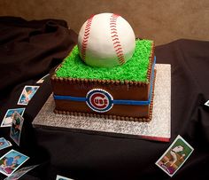 a cake that has a baseball in it on a table with cards and pictures around it