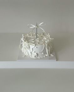 a white cake decorated with pearls, bows and a cross sitting on top of a shelf