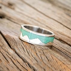 a silver ring with green and white designs on it sitting on a wooden table top