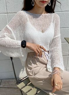 a woman sitting on top of a wooden bench wearing a white shirt and beige pants