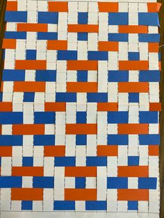 an orange, white and blue piece of paper is cut into squares on a wooden table