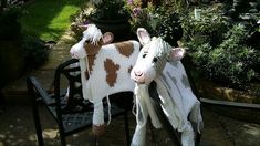 two knitted horses sitting on top of a chair in a garden with potted plants